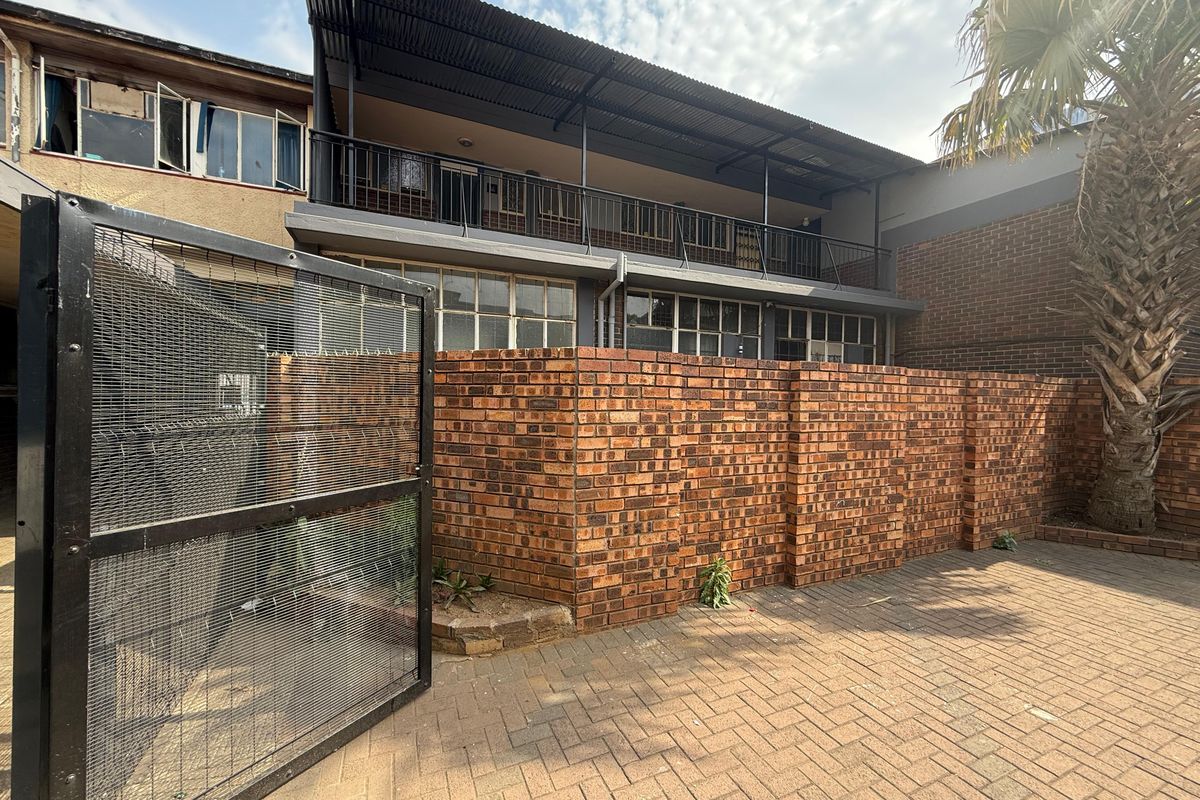 Rear exterior view of the office building featuring a paved courtyard, brick boundary wall, secure metal gate, and a covered upper-level balcony.