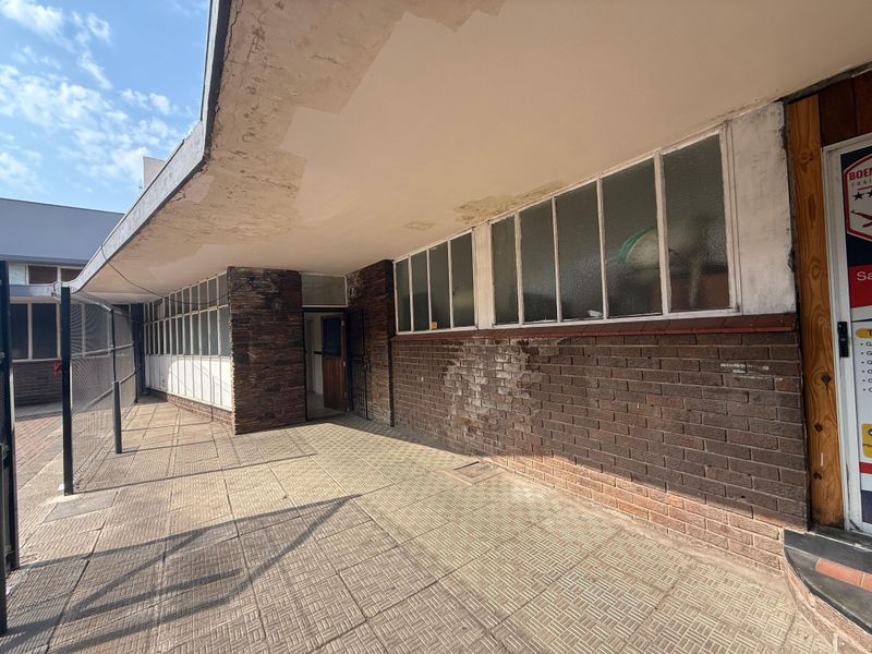 Exterior view of the office building entrance featuring a covered walkway, brick facade, and steel-framed windows with visible signs of weathering.