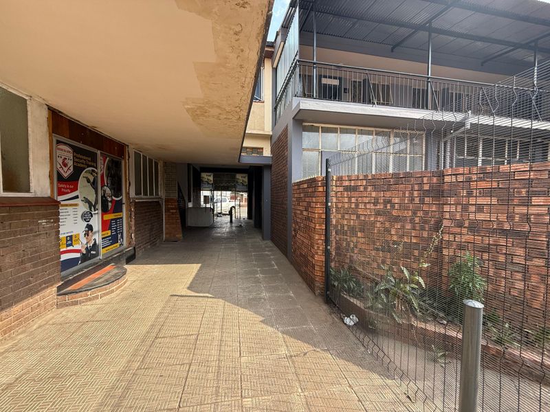 A covered exterior walkway between office building sections, featuring brick walls, paved flooring, and metal security fencing.