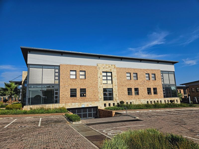 A modern multi-story office building featuring a face brick and stone facade, large windows with external shutters, and an underground parking entrance.