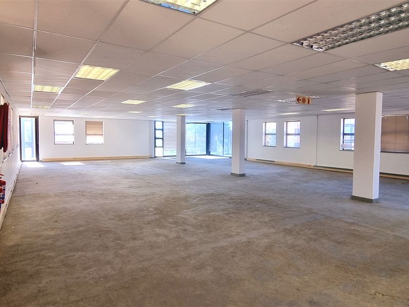 A large, open-plan office space featuring a suspended ceiling, recessed lighting, and structural columns, currently awaiting flooring installation and final fit-out.