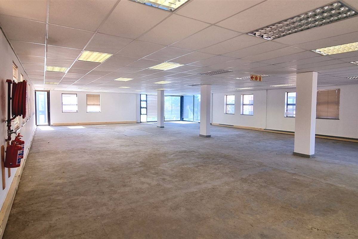 A large, open-plan office space featuring a suspended ceiling, recessed lighting, and structural columns, currently awaiting flooring installation and final fit-out.
