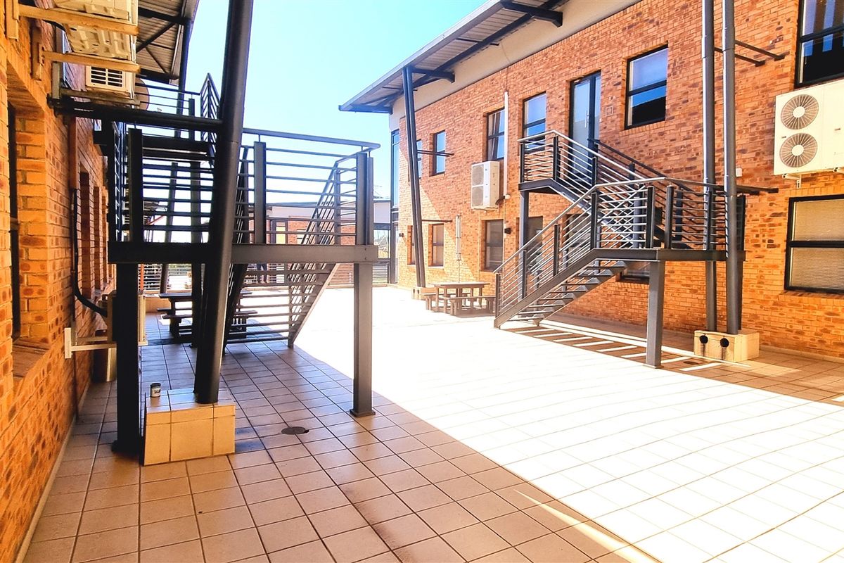 A spacious outdoor courtyard area featuring exposed brick office building facades, tiled flooring, and external metal staircases connecting the levels.