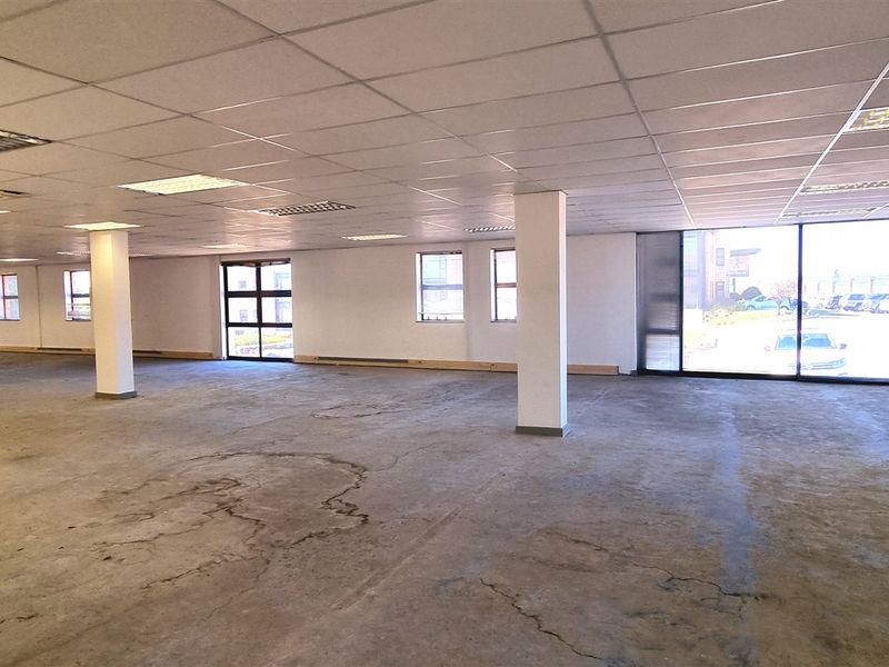 Spacious open-plan office area featuring large windows, structural columns, and a suspended ceiling, currently in need of flooring refurbishment.