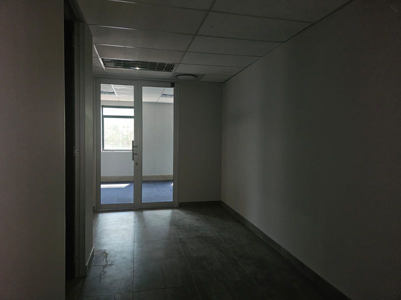 An empty office space featuring tiled flooring, a suspended ceiling, and a glass partition door leading to an adjacent room.
