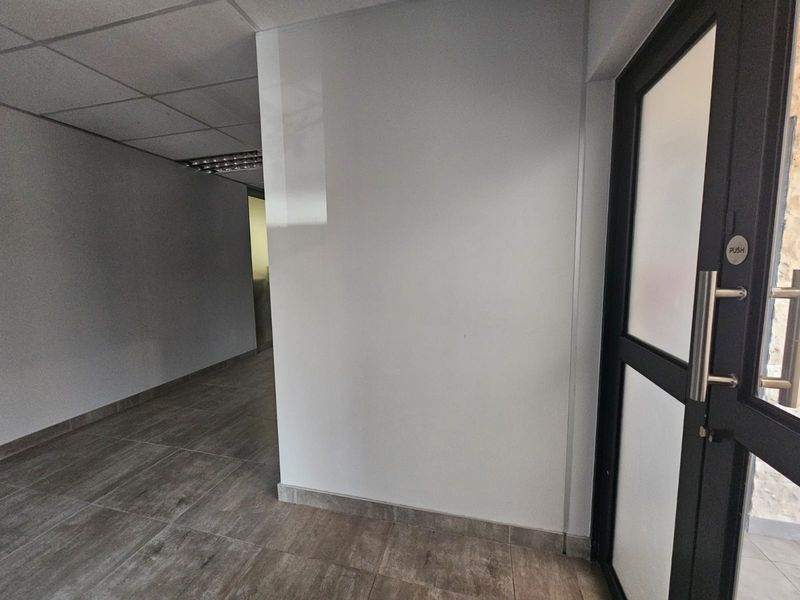A clean, empty entrance area featuring modern tiled flooring, a glass-panelled door, and a suspended ceiling with integrated lighting.