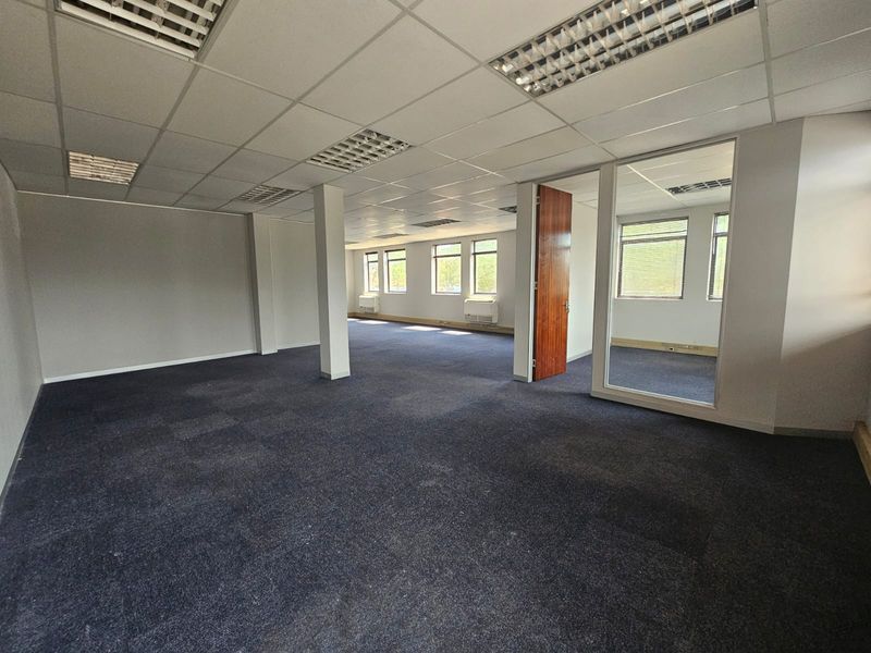 Spacious open-plan office area featuring suspended ceilings, recessed lighting, carpeted flooring, and a glass-partitioned private office space.