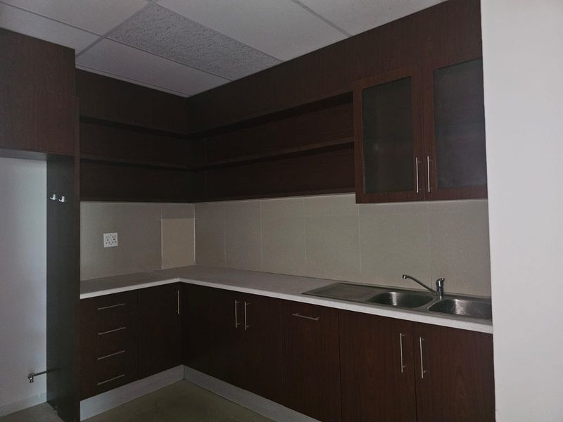 A functional kitchen area featuring dark wood cabinetry, ample storage, laminate countertops, and a double bowl stainless steel sink with a tiled backsplash.