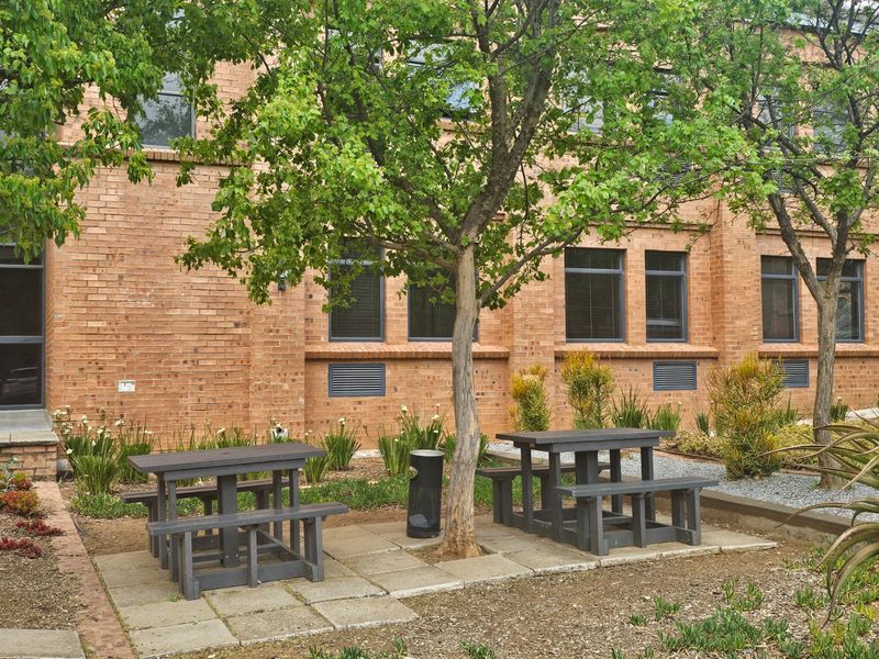 A well-maintained rear exterior area featuring a brick facade, paved seating sections, and established garden landscaping.