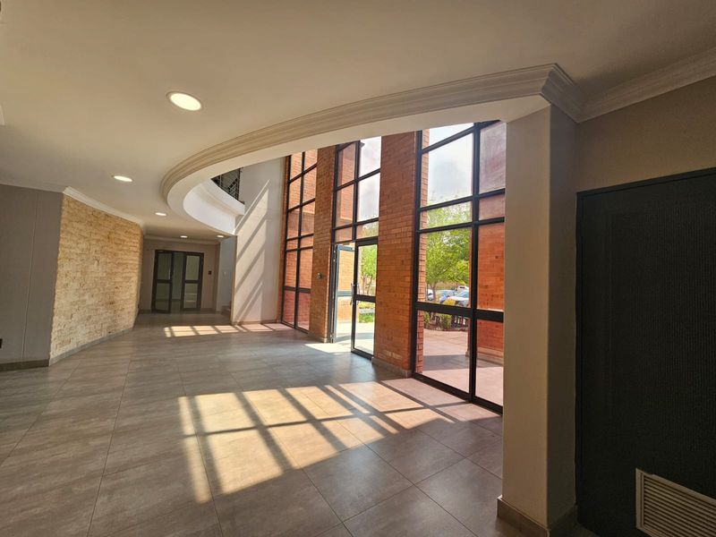 Spacious entrance lobby featuring high ceilings, exposed brickwork, a stone feature wall, and large floor-to-ceiling windows providing ample natural light.
