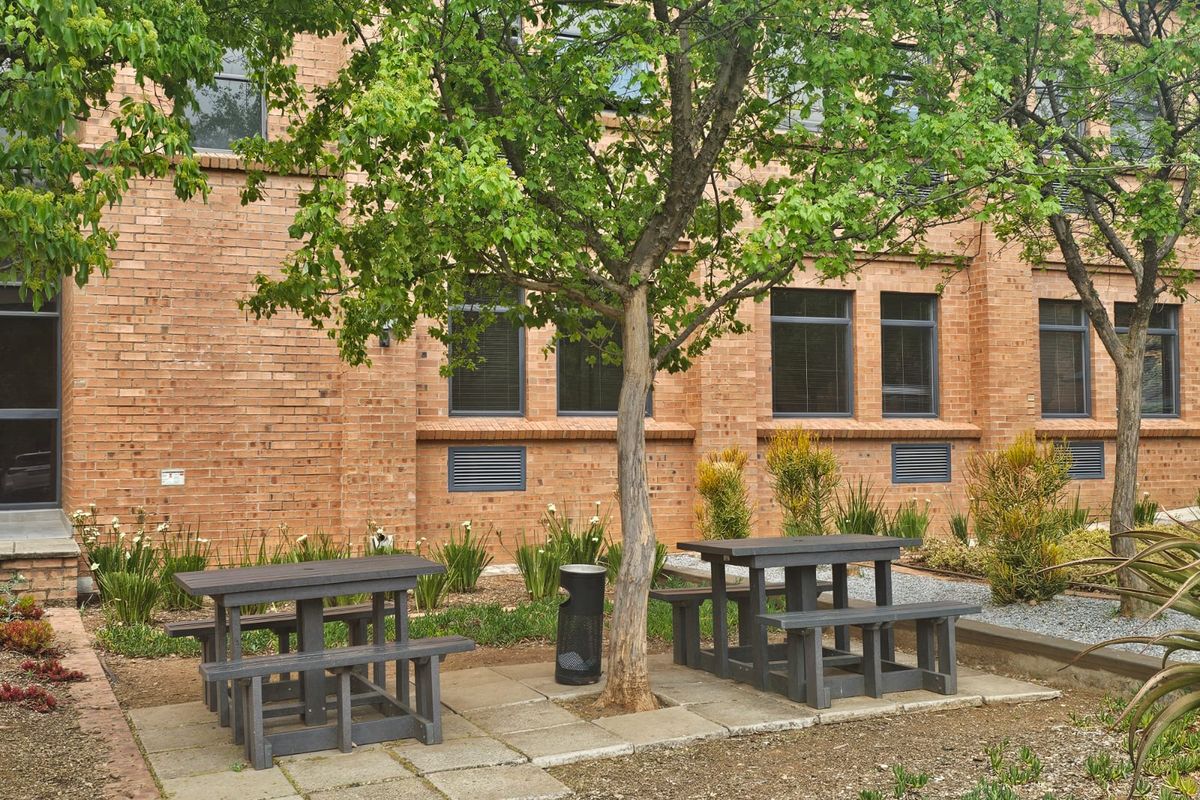 A well-maintained rear exterior area featuring a brick facade, paved seating sections, and established garden landscaping.
