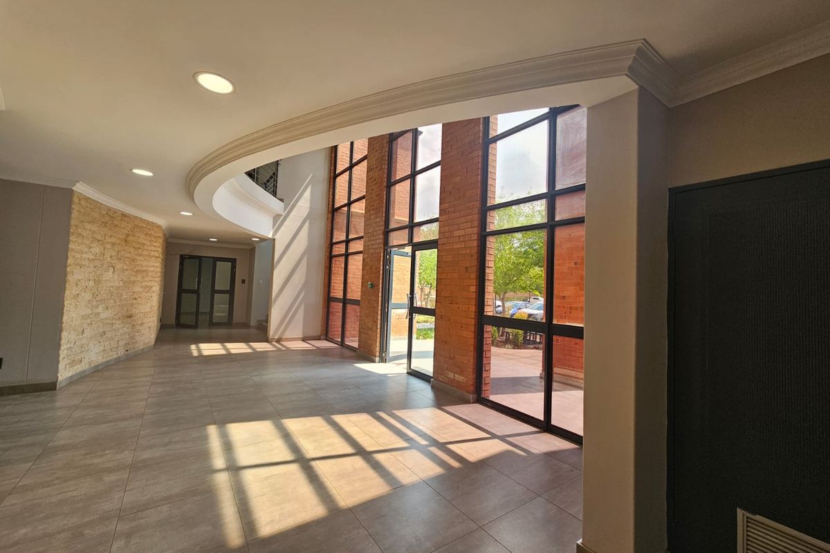 Spacious entrance lobby featuring high ceilings, exposed brickwork, a stone feature wall, and large floor-to-ceiling windows providing ample natural light.