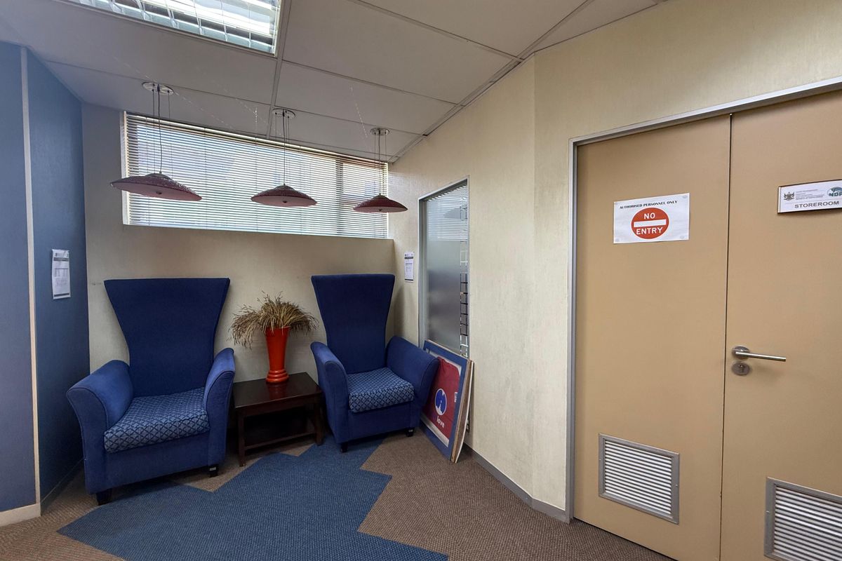 A functional office waiting area featuring a double door entrance to a storeroom, recessed ceiling lighting, and integrated window blinds.