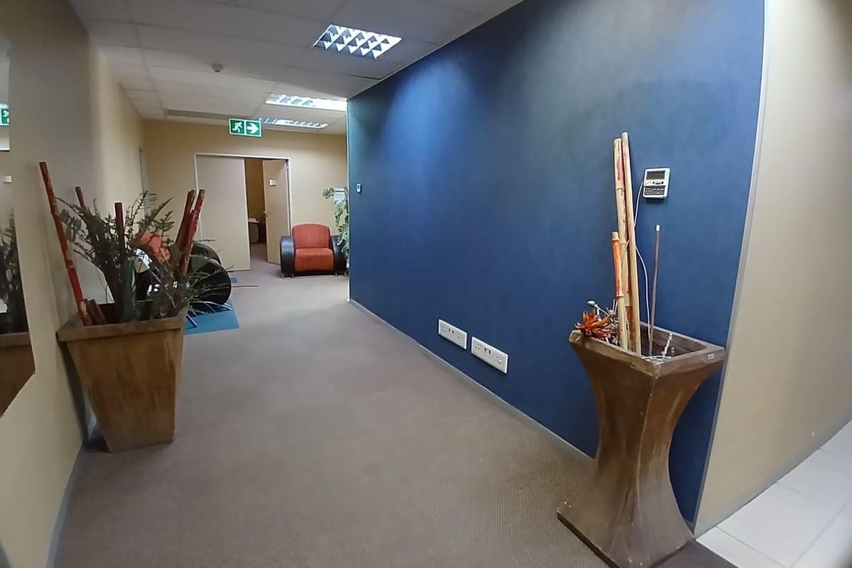 A commercial office hallway featuring a blue accent wall, recessed ceiling lighting, and carpeted flooring leading towards an office entrance.