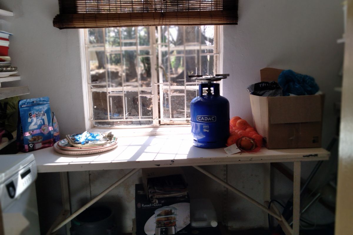A functional scullery or utility area featuring a window with security bars and a bamboo blind, providing natural light and workspace.