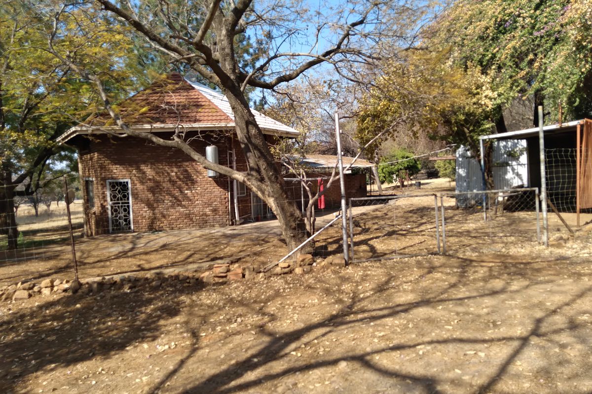Rear view of a face-brick dwelling featuring a tiled roof, security gate, and adjacent metal storage structure on a rural small holding.