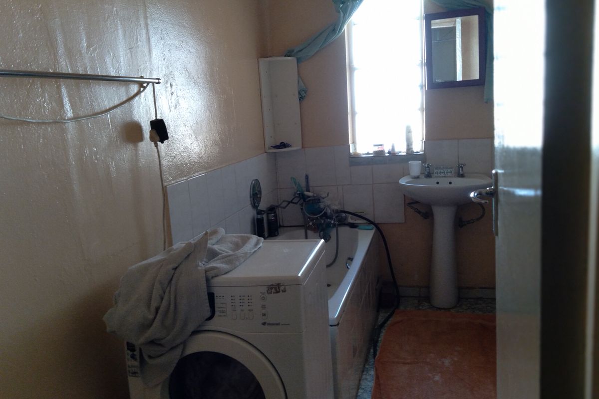 A compact bathroom featuring a pedestal basin and a bathtub, with tiled splashbacks and flooring. The space requires cosmetic updates to improve its condition.
