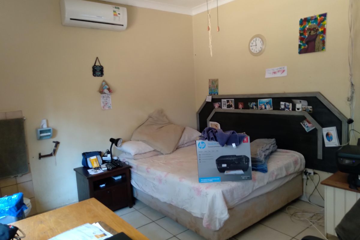 A bedroom featuring tiled flooring, a built-in headboard, and a wall-mounted air conditioning unit.