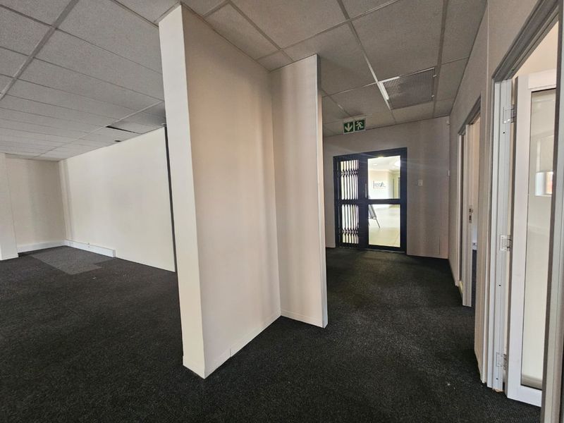 Empty commercial hallway featuring carpeted flooring, a suspended ceiling with minor damage, and a secure entrance gate.