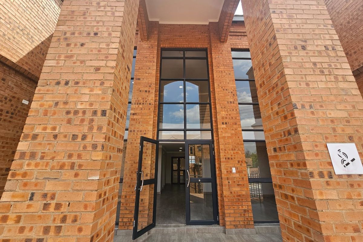 Modern commercial entrance featuring a double-volume face brick facade with large aluminium-framed glass doors and a tiled porch area.