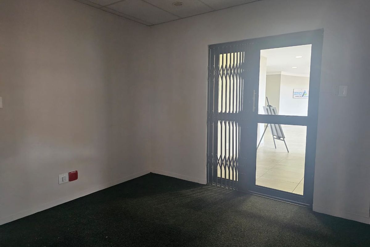 An empty office space featuring carpeted flooring, a suspended ceiling, and a secure glass entrance door with a metal security gate.