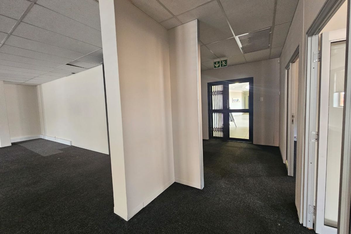 Empty commercial hallway featuring carpeted flooring, a suspended ceiling with minor damage, and a secure entrance gate.