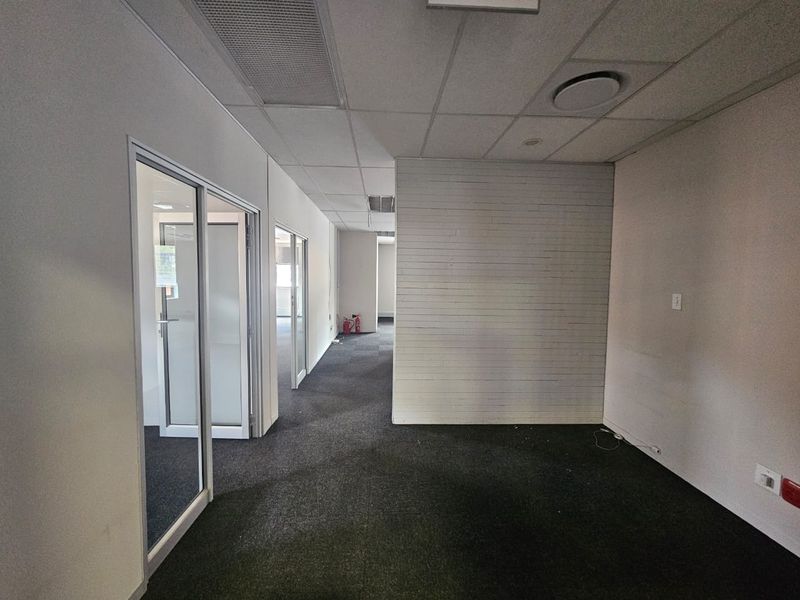 An empty office space featuring carpeted flooring, glass partition doors, and a suspended ceiling with integrated lighting and air conditioning vents.