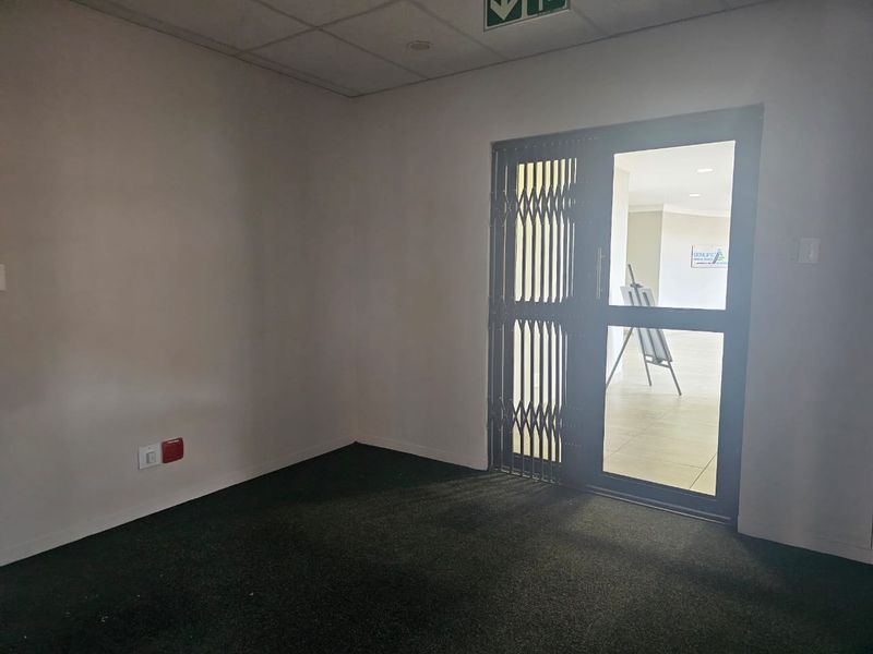 An empty office space featuring carpeted flooring, a suspended ceiling, and a secure glass entrance door with a metal security gate.