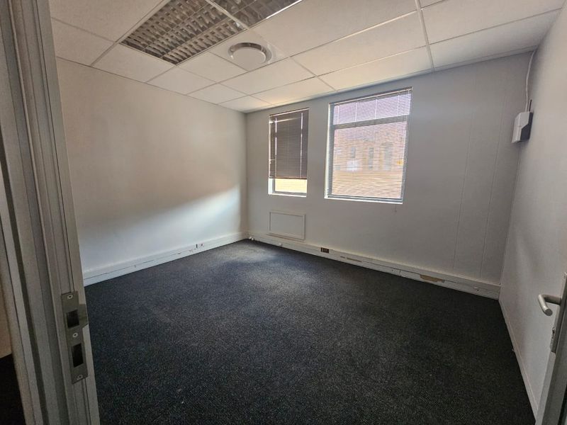 A vacant office space featuring a suspended ceiling, recessed lighting, carpeted flooring, and windows with fitted venetian blinds.
