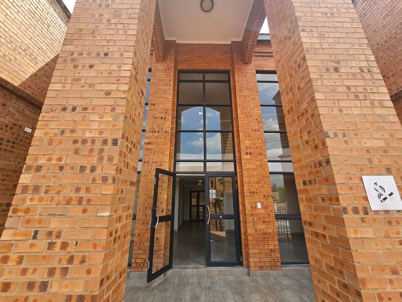 Modern commercial entrance featuring a double-volume face brick facade with large aluminium-framed glass doors and a tiled porch area.