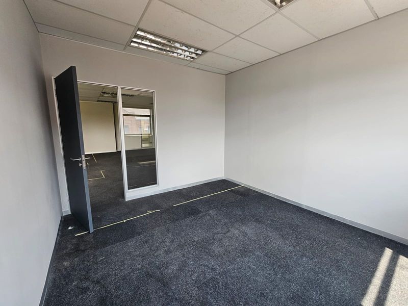 An empty office space featuring dark carpeting, a suspended ceiling with integrated lighting, and a glass partition wall.
