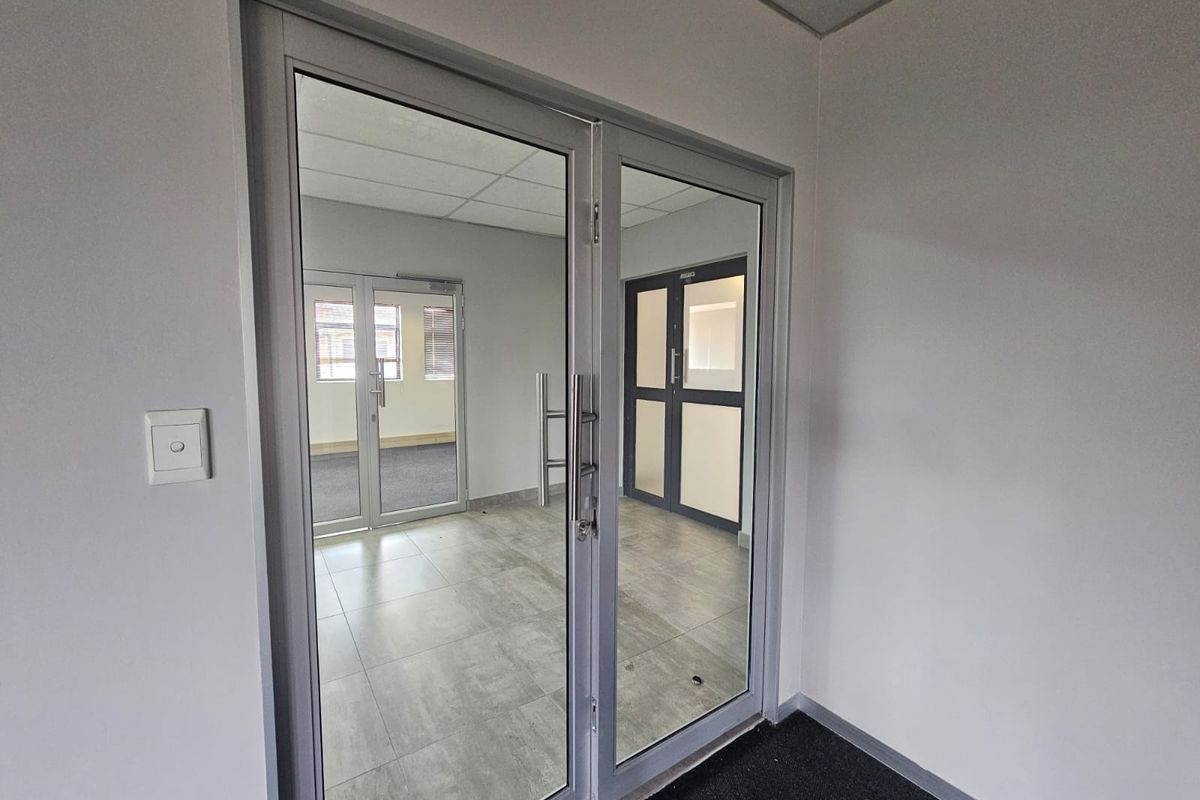 A clean, modern office entrance featuring glass double doors, tiled flooring, and a drop ceiling, providing a professional and bright welcome area.