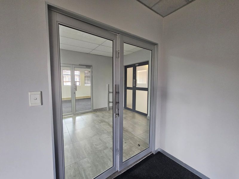 A clean, modern office entrance featuring glass double doors, tiled flooring, and a drop ceiling, providing a professional and bright welcome area.