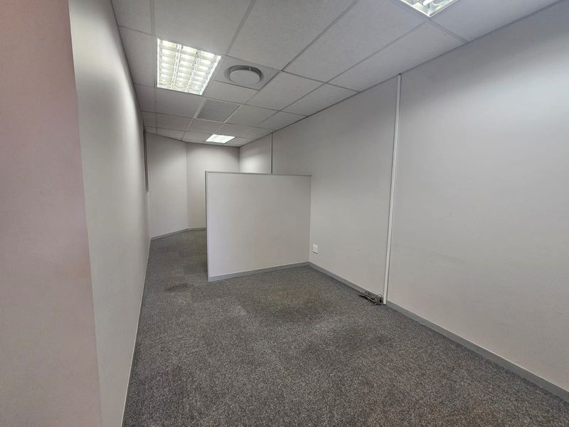 An empty office space featuring a partition wall, suspended ceiling with recessed lighting, and grey carpet flooring.