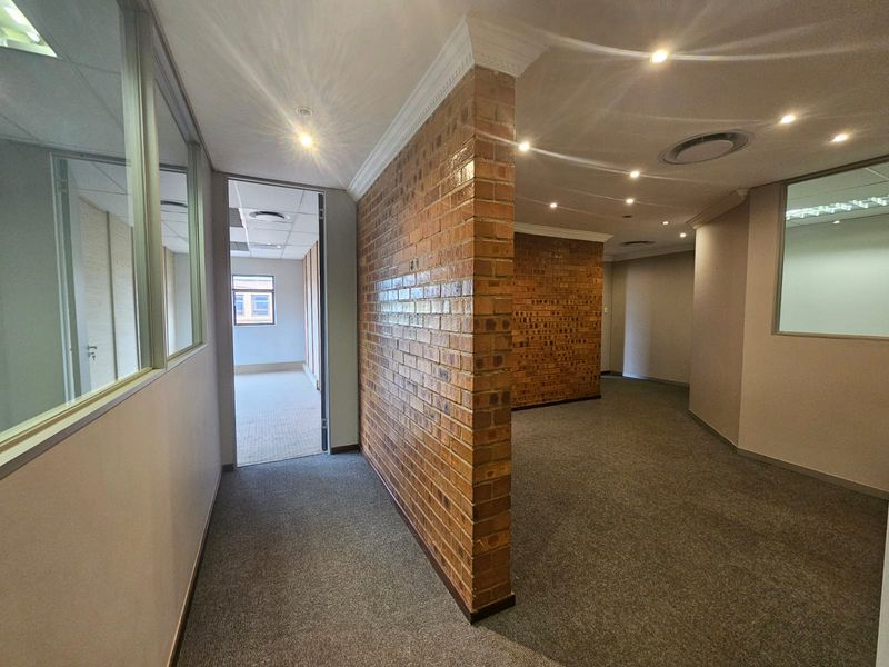 Modern office space featuring an exposed brick feature wall, glass partitions, recessed lighting, and neutral carpeting in a professional business environment.