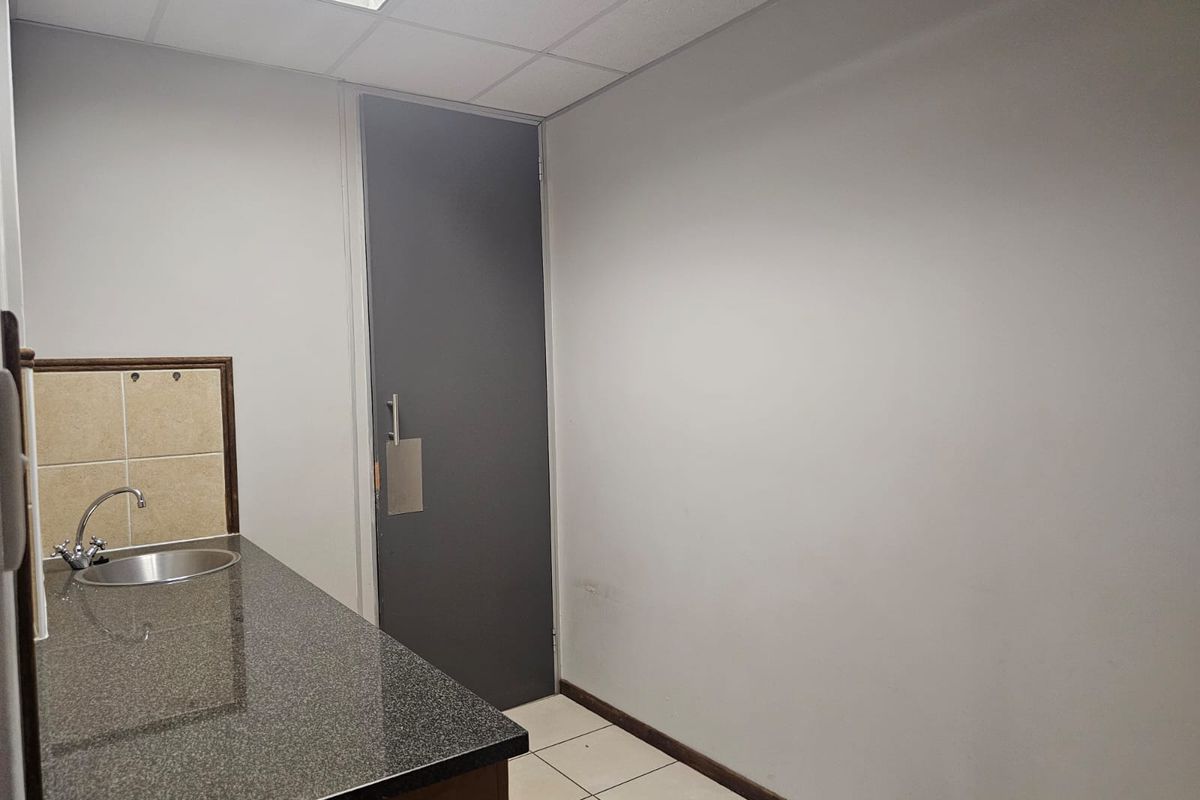 A compact, empty kitchenette featuring a granite countertop, stainless steel sink, tiled splashback, and neutral finishes, suitable for office or utility use.