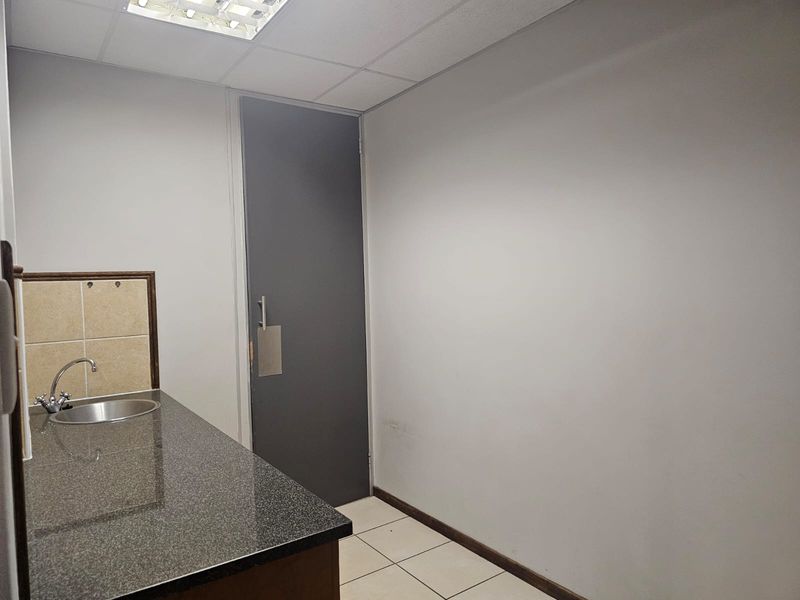 A compact, empty kitchenette featuring a granite countertop, stainless steel sink, tiled splashback, and neutral finishes, suitable for office or utility use.