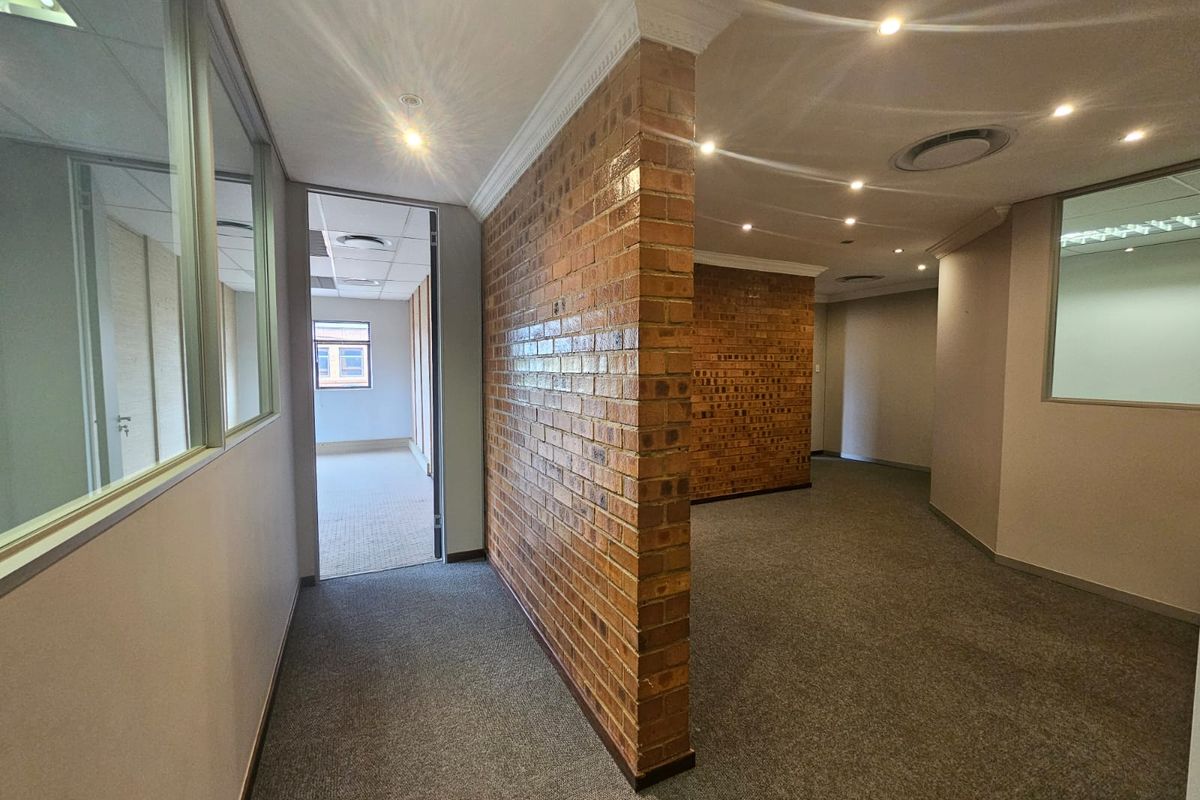 Modern office space featuring an exposed brick feature wall, glass partitions, recessed lighting, and neutral carpeting in a professional business environment.
