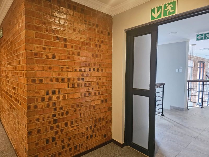 A clean hallway featuring an exposed brick wall, tiled flooring, and a frosted glass door with emergency exit signage.