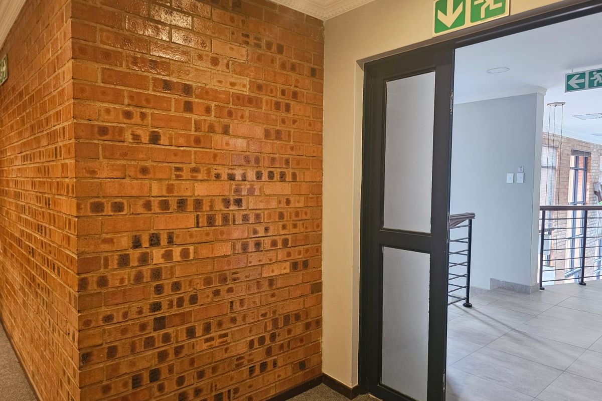 A clean hallway featuring an exposed brick wall, tiled flooring, and a frosted glass door with emergency exit signage.