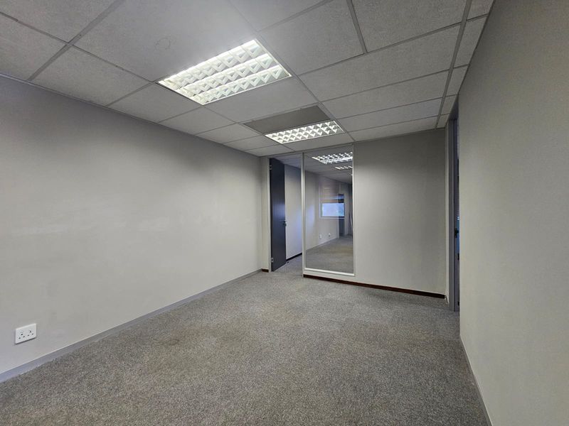 A vacant, carpeted office space featuring a suspended ceiling with recessed lighting and a glass partition wall, suitable for a professional workspace.