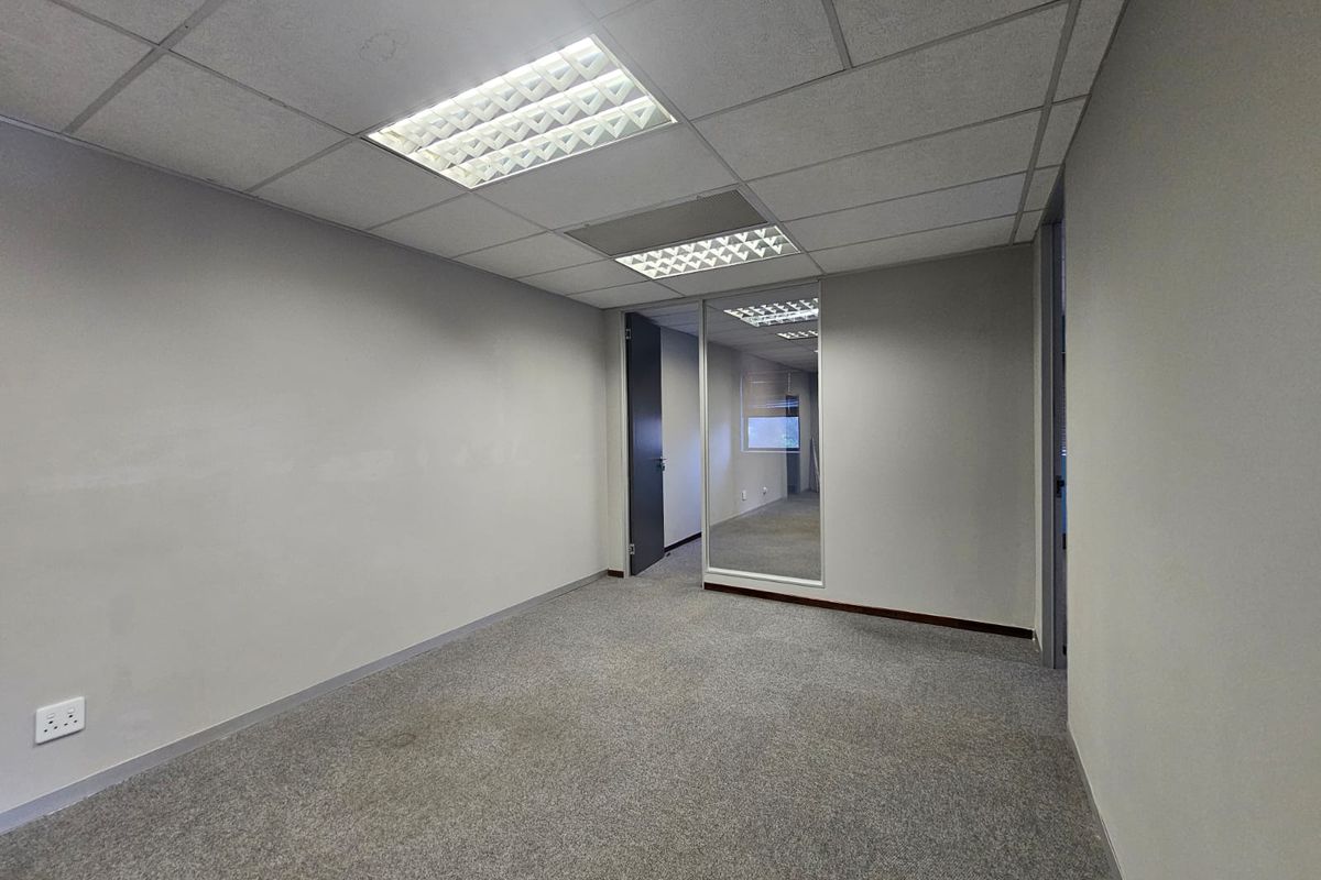 A vacant, carpeted office space featuring a suspended ceiling with recessed lighting and a glass partition wall, suitable for a professional workspace.