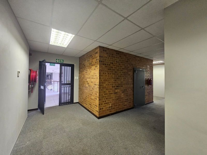A functional commercial hallway featuring a suspended ceiling, exposed brick feature wall, and integrated fire safety equipment including a hose reel and extinguisher.