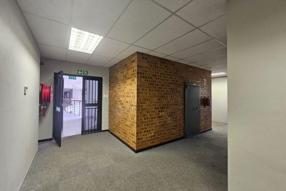 A functional commercial hallway featuring a suspended ceiling, exposed brick feature wall, and integrated fire safety equipment including a hose reel and extinguisher.