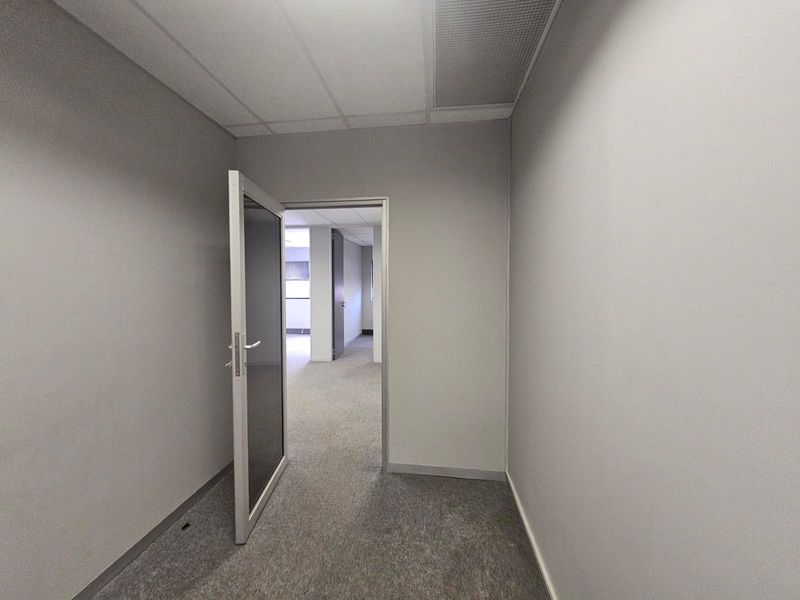 A vacant office space featuring neutral grey walls, carpeted flooring, and a suspended ceiling with integrated air conditioning ventilation.