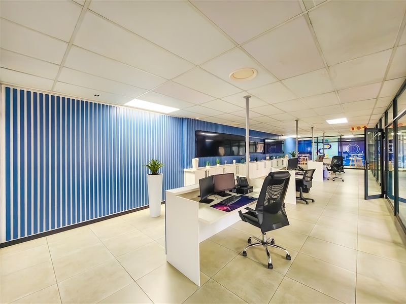 Modern open-plan office space featuring tiled flooring, a suspended ceiling, and integrated cabinetry with glass partition walls.