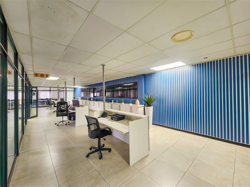 Open-plan office space featuring tiled flooring, suspended ceilings, glass partitions, and built-in storage cabinetry along the blue feature wall.
