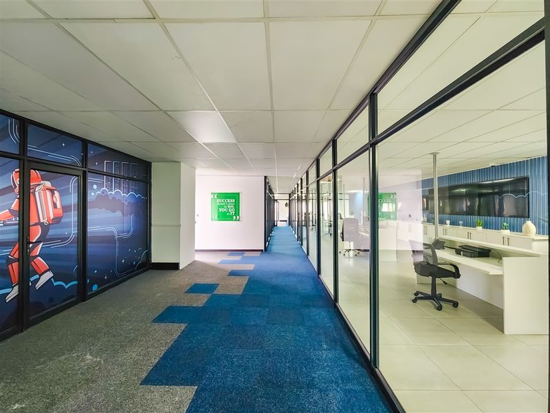 A modern office hallway featuring glass partition walls, a mix of carpet and tile flooring, and a built-in reception area.
