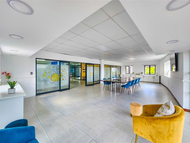 Spacious modern office area featuring glass partitions, suspended ceiling tiles, recessed lighting, and neutral tiled flooring, providing a bright and professional workspace.
