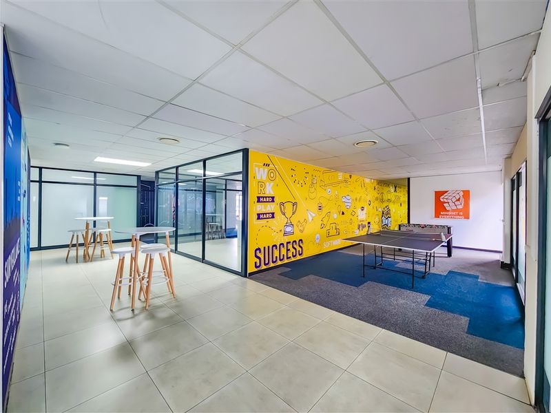 Modern open-plan office breakout area featuring glass-partitioned meeting rooms, suspended ceilings, and a mix of tiled and carpeted flooring.